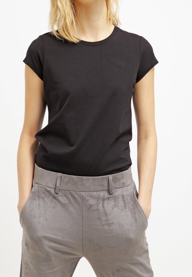 Femme portant un t-shirt noir ajusté à manches courtes, rentré dans un pantalon en satin gris taille haute, les mains dans les poches.