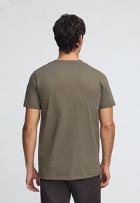 T-shirt en coton vert olive à manches courtes et col rond, présentant une texture lisse et une coupe décontractée. Sans logos ni motifs visibles.