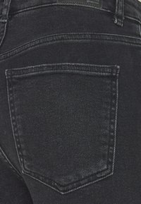 Černé džínové kalhoty s zadní kapsou. Materiál má hladkou strukturu s jemným vyblednutím a kontrastním švem podél švů.