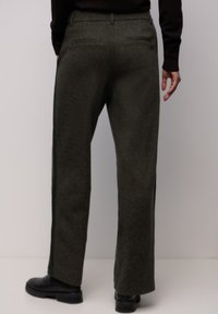 Olijfgroene broek met een gestructureerde stof, rechte pasvorm en zijopeningen. Heeft twee achterzakken en wordt gedragen met zwarte schoenen.