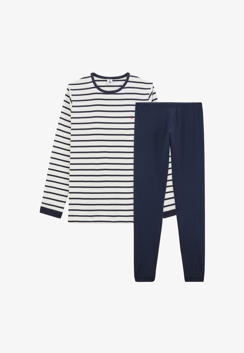 Bela majica z dolgimi rokavi s črnimi vodoravnimi črtami, kombinirana z enobarvnimi temno modrimi legicami, položena na ravno belo podlago.