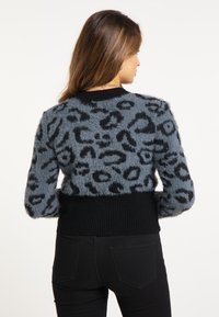 Leopardprint sweater i grå og sort, med en fluffy tekstur og ribbet sort talje. Lange ærmer med mønstret detaljer.