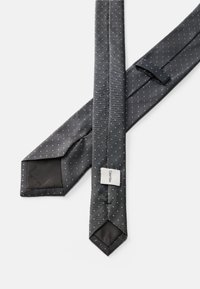 Musta solmio, jossa on pieniä valkoisia pilkkuja. Valmistettu teksturoidusta kankaasta, jolle on ominaista terävä pää ja etiketti. Takaosa on sileä.