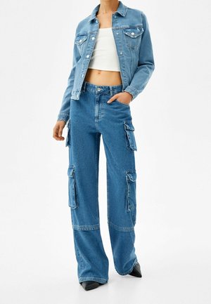 Lyseblå denimjakke med to brystlommer, parret med brede cargobukser med sidelommer og høj talje.