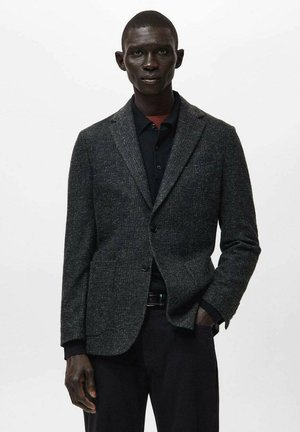 Dunkelgrauer Blazer aus strukturiertem Stoff, mit Reverskragen, Ein-Knopf-Verschluss und Fronttaschen, kombiniert mit einem schwarzen Hemd.