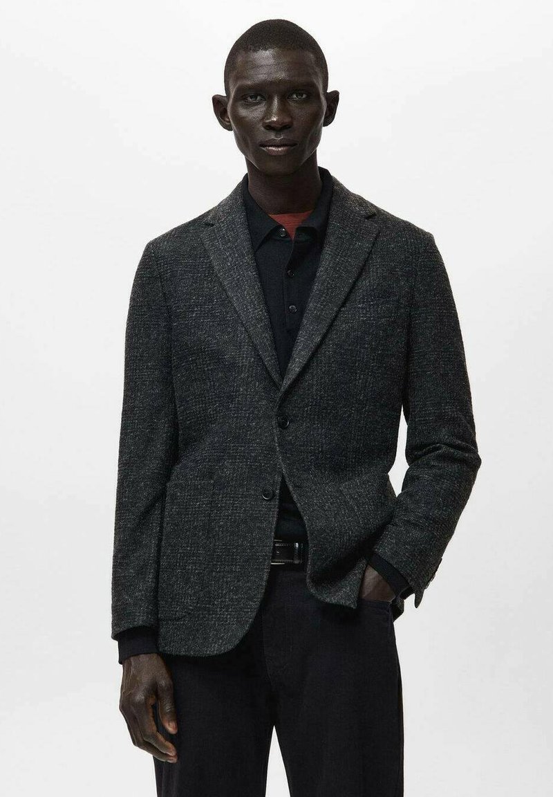 Dunkelgrauer Blazer aus strukturiertem Stoff, mit Reverskragen, Ein-Knopf-Verschluss und Fronttaschen, kombiniert mit einem schwarzen Hemd.