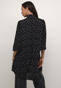 Must have kolmveerandise varrukaga must blouse, millel on valged ja helesinised täpid. Loodud mugavaks seljast, kõrge kaelusega ja ümara hemiga.