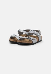 Sandali silver glitter con cinturini regolabili, suola in sughero e suola in gomma nera texturizzata. Presentano fibbie per una vestibilità sicura.