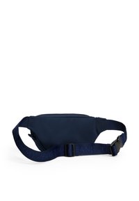 Τσαντάκι μέσης από ύφασμα σε ναυτικό μπλε χρώμα με ρυθμιζόμενο ιμάντα που φέρει το κείμενο "Tommy Jeans" και μαύρο πλαστικό κούμπωμα, σε λευκό φόντο.