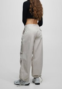 Lichtgrijze, losse cargobroek met een trekkoord onderaan, voorzien van zijzakken en een zachte, gebreide stof. Gepaarde met sportschoenen.