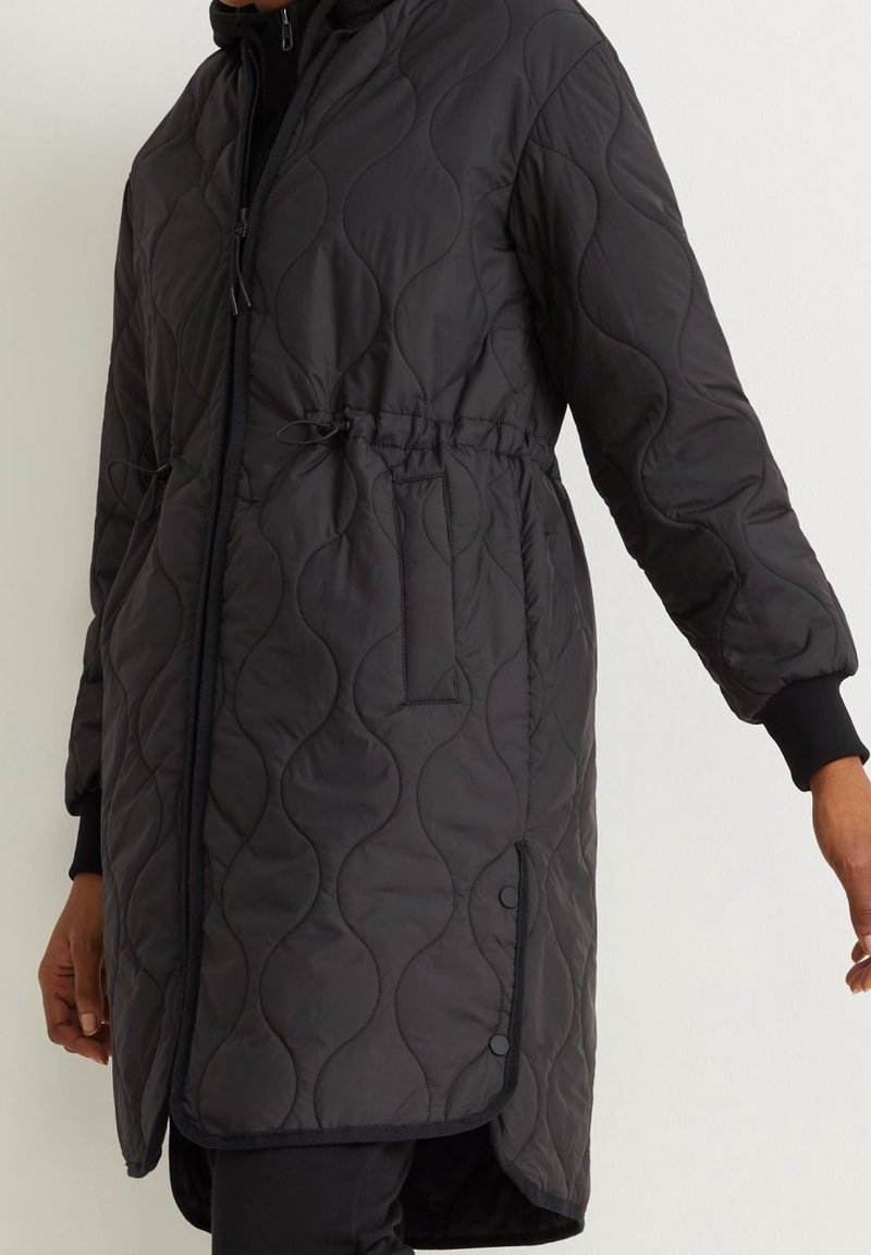 Giacca nera trapuntata con vita regolabile con coulisse, cappuccio e bottoni laterali. Il materiale ha una texture liscia con motivo a onde.