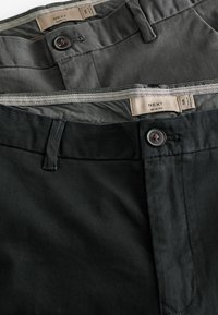 Kaks paari slim-fit pükse tumedas hallis ja mustas. Igal paaril on nööbiga sulgemine ja kontrastne vöökoht koos brändi märgistusega.