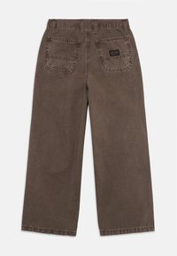 Pantaloni ampi marroni con tasche posteriori a toppa, una delle quali presenta un piccolo etichetta nera del marchio, esposti piatti su uno sfondo bianco.