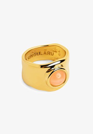 Złoty pierścionek z gładką, zakrzywioną obrączką, ozdobiony dużym okrągłym, jasnopomarańczowym kamieniem osadzonym w wypolerowanej oprawie. Oznaczony napisem "SINGULARU."