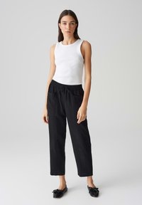 Witte geribde tanktop gecombineerd met zwarte relaxte broek met een elastische tailleband en zijzakken. Draag het met zwarte flats.