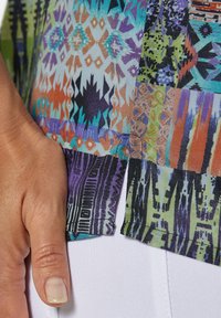 Bunt gemustertes Stoffgewebe mit geometrischen Designs in Blau, Orange, Grün und Lila, mit einer leichten Textur und einem seitlichen Schlitzdetail.