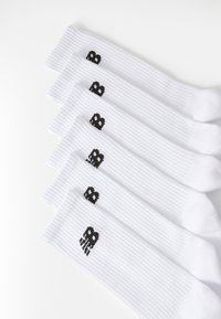 Λευκές βαμβακερές κάλτσες με ριγέ υφή, που διαθέτουν σχέδιο με μια μαύρη καρδιά και πλοκή που εκτυπώνεται στον αστράγαλο. Πέντε ζεύγη τοποθετημένα σε σειρά.