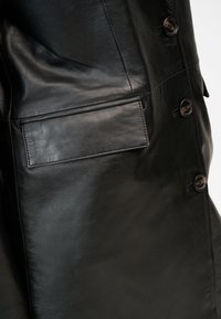 Svart läderjacka med en slät yta, framknappar och en rektangulär ficka med sydda kanter.