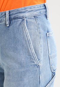 Ljusblå denimshorts med hög midja, med framträdande sömnader, sidofickor och en något slitagen yta.