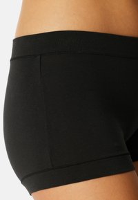 Svarta stretchiga bomullsshorts med en mjuk midja, med en slät textur och enkel design som framhäver fållen och sömmarna.