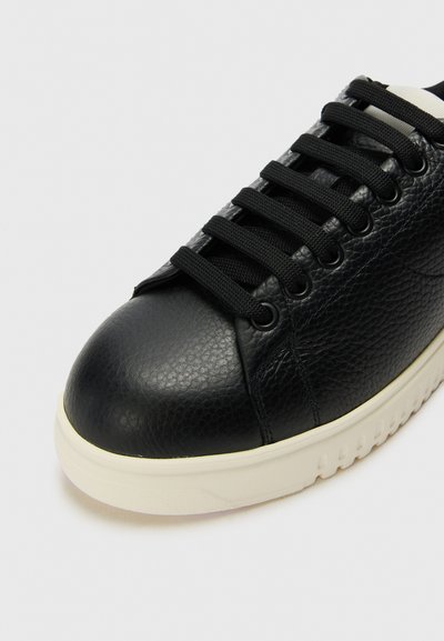 Svart lädersneaker med strukturerad yta, som har svarta snören och en vit gummisula. Rund tå och minimalistisk design.