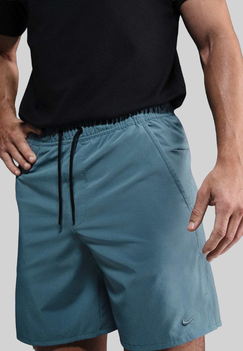 Lyseblå sportsshorts med elastisk talje, snor, sidelommer og et lille sort Nike-logo nederst til venstre.
