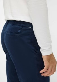 Marineblaue Hosen mit weicher Textur, elastischem Bund und Seitentaschen. Ein kleines Markenetikett ist auf der Rückseite sichtbar.