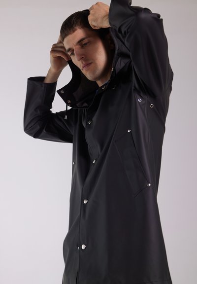 Black waterproof raincoat with a hood, snap-button closure, side pocket, and grommet details, featuring a smooth, sleek texture.