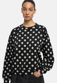 Czarny sweter z białymi kropkami, z raglanowymi rękawami, okrągłym dekoltem oraz ściągaczami przy mankietach i u dołu. Wykonany z miękkiej mieszanki bawełny.
