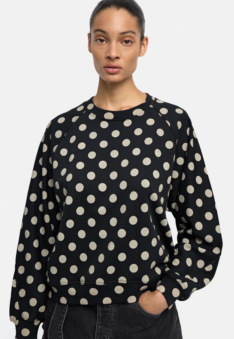 Czarny sweter z białymi kropkami, z raglanowymi rękawami, okrągłym dekoltem oraz ściągaczami przy mankietach i u dołu. Wykonany z miękkiej mieszanki bawełny.