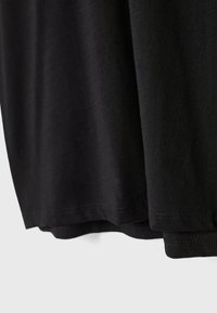 T-shirt en coton noir avec une texture douce, coupe droite et détails de couture à l'ourlet. Design simple sans motifs ni accents supplémentaires.