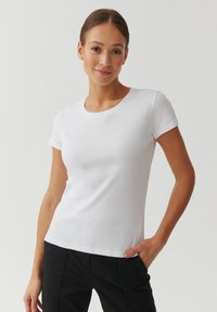 Valkoinen lyhythihainen slim fit t-paita, joka on valmistettu pehmeästä puuvillasta. T-paidassa on pyöreä pääntie ja sileä rakenne, ja se on yhdistetty mustiin housuihin.