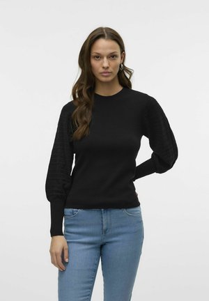 Maglione nero a collo rotondo con maniche a palloncino texture, polsini aderenti. Abbinato a jeans in denim blu chiaro.