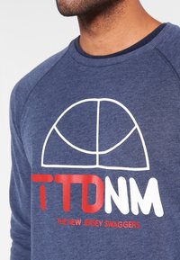 Mörkblå sweatshirt med vit och röd grafisk text. Har rundad halsringning och raglanärmar, tillverkad av mjukt strukturerat tyg.