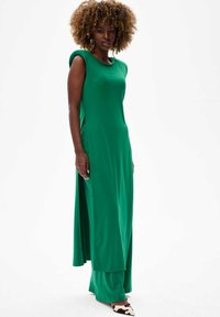 Groene maxi-jurk met korte mouwen en zijsplits, gemaakt van een gladde stof. Gecombineerd met gestreepte schoenen voor contrast.