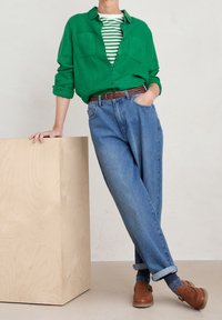 Groene linnen overhemden met knopen, gelaagd over een wit en groen gestreept shirt, gecombineerd met lichtblauwe hooggetailleerde spijkerbroeken en bruine geweven schoenen.