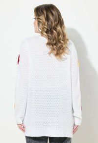 Cardigan bianco lavorato a maglia con una trama aperta, caratterizzato da accenti floreali colorati sulle maniche e polsini a coste. Texture morbida e design di lunghezza media.