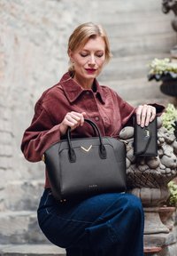 Black structured handbag with a gold accent and logo, paired with a sleek black wallet, against a textured stone backdrop.