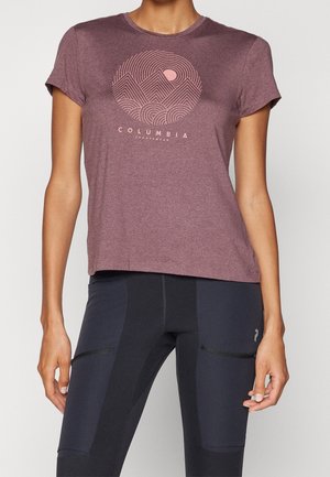 Vrouw draagt een mauve Columbia Sportswear T-shirt met berggrafiek en zwarte sportleggings met voorzakken.