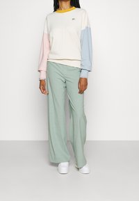 Sudadera de crema clara con mangas en tonos rosa y azul pastel, y cuello amarillo. Pantalones verdes menta de pierna ancha y zapatillas blancas. Diseño sencillo.