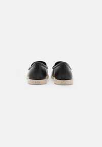 Mustat nahkaiset slip-on-kengät, joissa on sileä pinta, pyöreä muoto, beige kumipohja ja minimalistinen muotoilu.