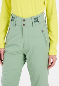Lichtgroene sneeuwbroek met een gladde textuur, voorzien van twee ritszakken, een knoopsluiting en contrasterende details op de tailleband.