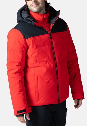 Chaqueta aislante roja con acentos negros, diseño acolchado, cierre completo, bolsillos con cremallera y puños ajustables. El tejido parece suave y duradero.