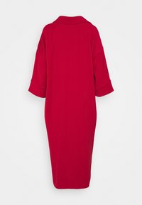 Robe rouge longueur genou en tissu lisse, avec un col à revers et des manches larges retroussées. Design simple et épuré.