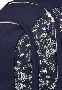 Sac à dos bleu marine avec motif floral comprenant des fleurs blanches et des tiges vertes. Deux tirettes de fermeture éclair de la marque Satch sont visibles. Texture de tissu durable.