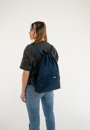 Mochila de cordón en navy, fabricada con un material duradero, que cuenta con correas ajustables y un pequeño logo en el frente. Textura suave y diseño simple.