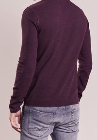 Burgundyfärgad långärmad stickad topp med en figurnära design. Har en rundad halsringning och strukturerad tyg, kombinerat med grå jeans med bakfickor.