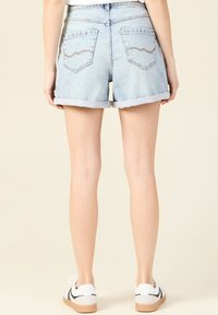 Vaaleansiniset farkkushortsit, joissa on käärityt lahkeet ja kaksi takataskua, joissa on kirjontakuvio aaltoina. Yhdistetty valkoisiin ja mustiin tennareihin.