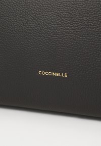 Sort læderpung med en tekstureret overflade, der har et guld "Coccinelle"-logo. Enkel design, kompakt form og holdbart materiale.