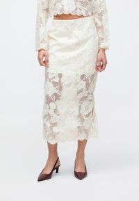 Doorzichtige bloemenkant rok in off-white met een geschulpte zoom en een aansluitend silhouet, gecombineerd met bordeauxrode pumps met puntige neus.